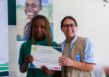 Two women smile while holding a certificate in a celebratory setting.