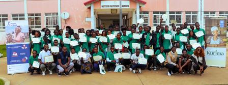 A large group of people in green shirts holding certificates, gathered outside a building.