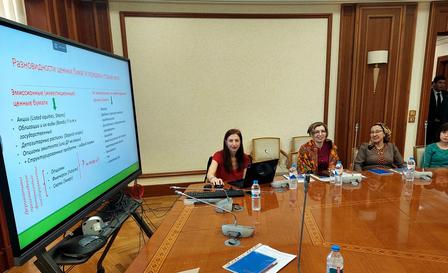 A woman presents at a large screen while three others listen at a conference table.