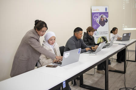 A group of individuals working on laptops at a conference table, focused on their tasks.