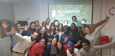 Group photo of smiling individuals with hands raised, celebrating in a bright office space.