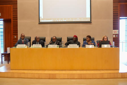 Panel discussion with six speakers in a formal setting, seated at a long table.
