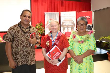 Three individuals smile together in a colorful setting, adorned with floral leis.