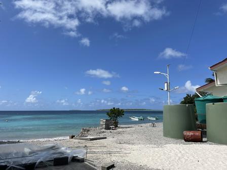 Coastal scene with sand, water, green tanks, and a clear blue sky.