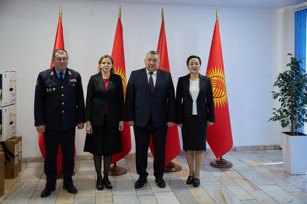 Four officials stand in a room with national flags, dressed in formal attire.
