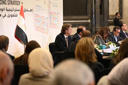 A meeting with several individuals seated, a flag of Egypt visible in the background.