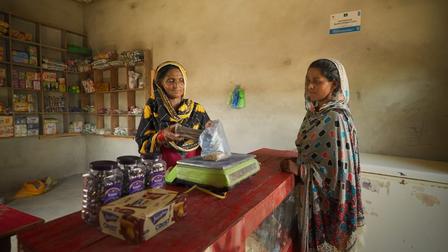 A shopkeeper hands a bag to a customer at a small, cluttered store.