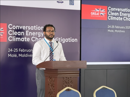 A man in a white shirt stands at a podium during a conference on clean energy.