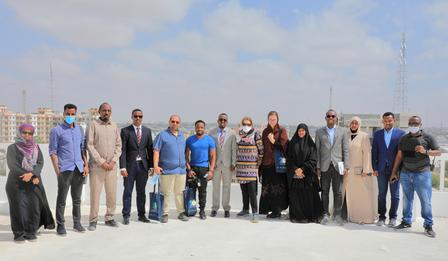 A diverse group of people standing together outdoors, smiling against a cloudy sky.