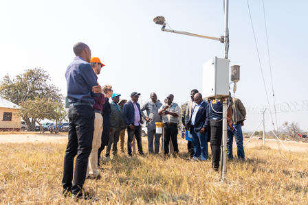 A group of people gathered around a weather station in a grassy field.