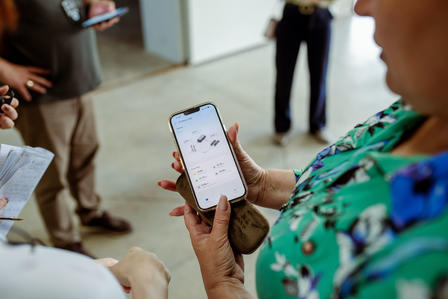 A person holding a smartphone displaying an app, surrounded by others in a casual setting.