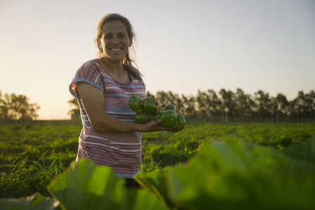 Woman smiling while holding green apples in a field at sunset.
