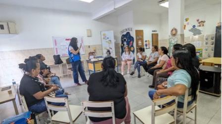 A group discussion in a bright room, with a speaker presenting to seated participants.