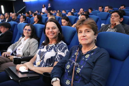 Three women seated in a theater, smiling, with an audience visible in the background.