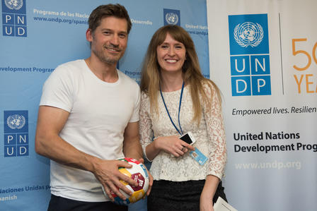 Two people pose together, smiling, holding a soccer ball in an event setting.