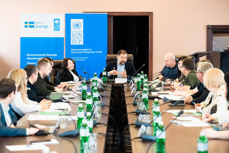 A conference room with participants seated around a long table, engaged in discussion.