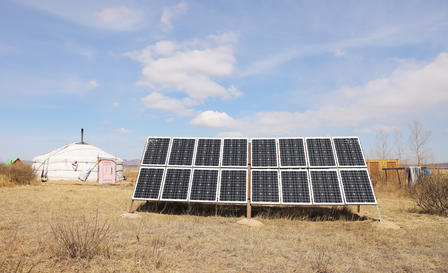 Solar panels installed outdoors beside a white yurt under a blue sky.