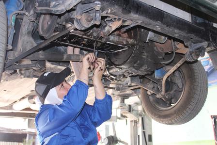 A mechanic working under a car, using tools to perform repairs.