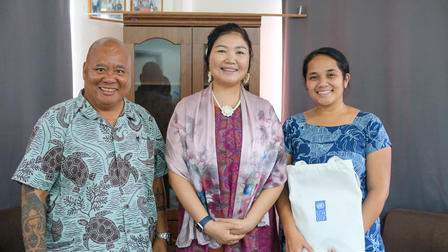 Three individuals pose together, smiling, in a warmly lit indoor setting.