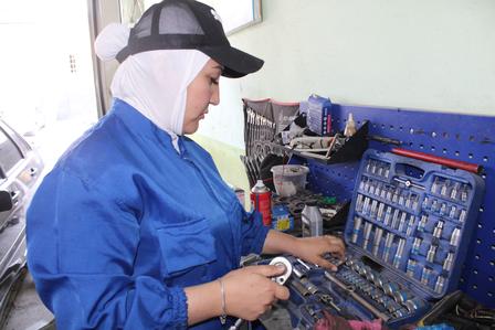 A woman in a blue work uniform examines tools in a mechanic's workshop.