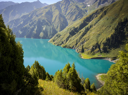 Serene lake surrounded by lush green mountains under a clear blue sky.