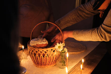 A person places a decorated cake into a wicker basket on a dimly lit table.