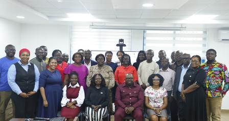 A diverse group of people stands together in a bright meeting room, smiling.