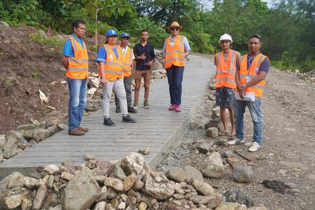 Seven construction workers in safety gear stand on a newly built path among rocky terrain.