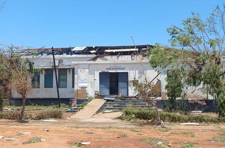 Damaged building with a missing roof, surrounded by sparse vegetation and clear blue sky.
