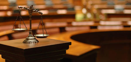 A scale representing justice sits on a wooden podium in an empty courtroom.