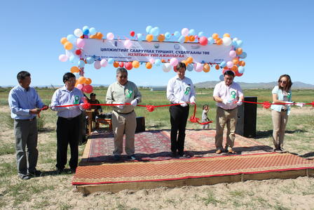 Five individuals at a ribbon-cutting ceremony with balloons and decorations in an outdoor setting.