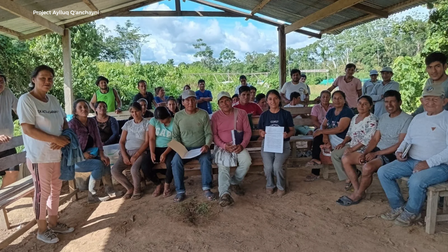 A diverse group of people gathered under a shelter in a green outdoor setting.