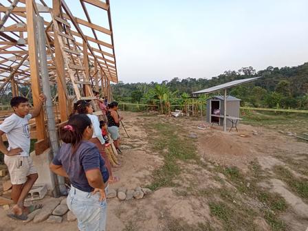 A group of people standing near a building framework, with a solar panel in the background.