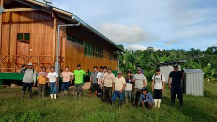Group of diverse people posing in front of a wooden building in a green field.