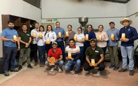 A group of diverse individuals holds up coffee packets in a warehouse setting.