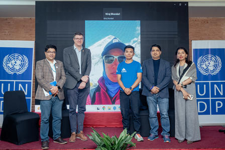 Five people stand in front of a screen displaying a person in outdoor gear.