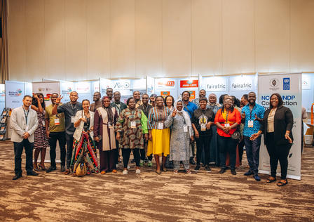 A diverse group of people poses together in a conference setting, smiling cheerfully.