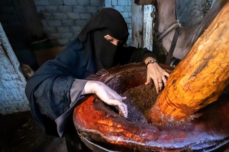 A woman in a black garment uses a large wooden mortar to grind spices.