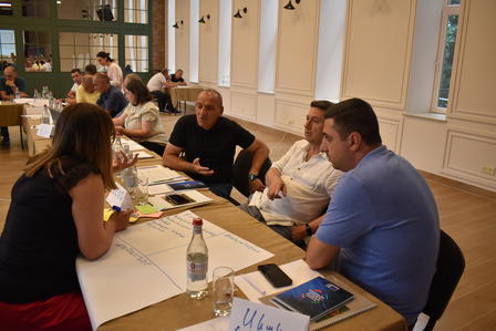 A group of four people discussing around a table in a bright, spacious room.