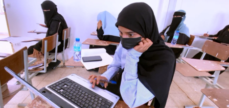 Student in a hijab working on a laptop in a classroom, focused and engaged.