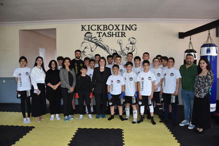 A group photo of young kickboxers and coaches in a training gym, smiling together.