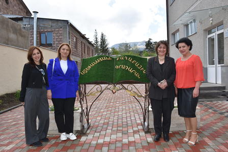 Four women stand together in front of a green decorative arch on a cobblestone path.