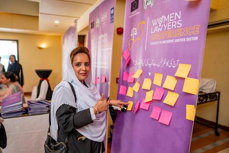 Woman in a hijab places sticky notes on a conference board in a bright, welcoming room.