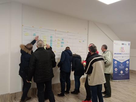 Group of people interacting with a wall chart in a well-lit indoor space.