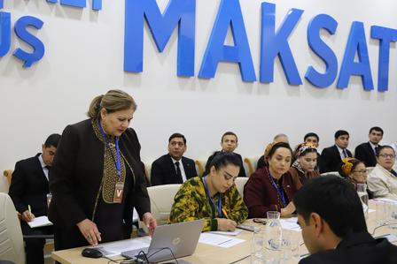 A woman speaks at a conference table with several attentive participants.