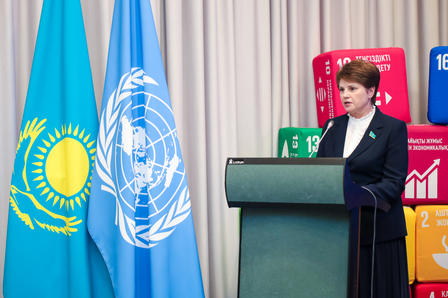 A woman speaks at a podium with the Kazakhstan and UN flags in the background.