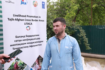 A man in a light blue jacket stands in front of a promotional banner outdoors.
