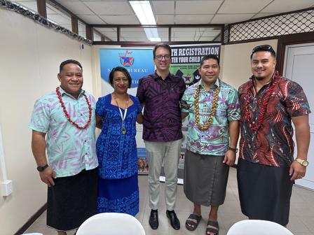 Five individuals pose together, wearing colorful traditional attire, in a bright room.