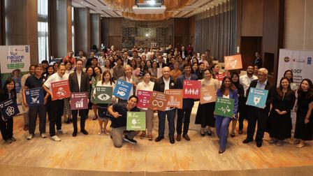 A diverse group of individuals poses together holding colorful signs in a large indoor space.