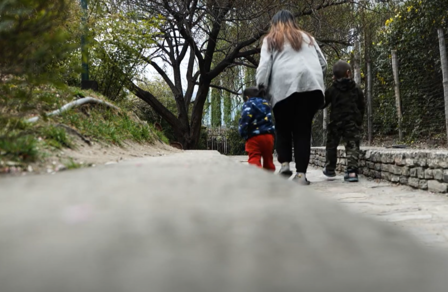 A woman and two children walk along a path surrounded by greenery.